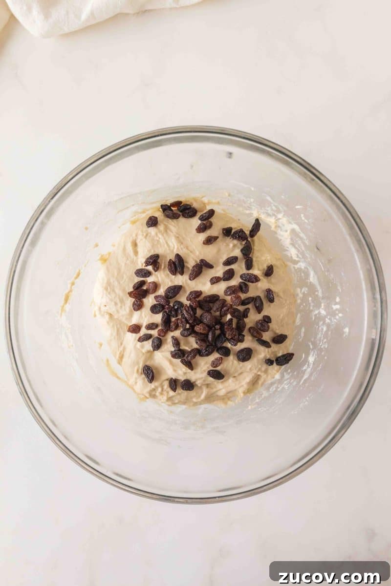 Sourdough Cinnamon Raisin Bread Recipe — Soft, Sweet & Spiced 7 Sticky sourdough bread dough in a mixing bowl with dark raisins on top ready for folding. Hostess At Heart