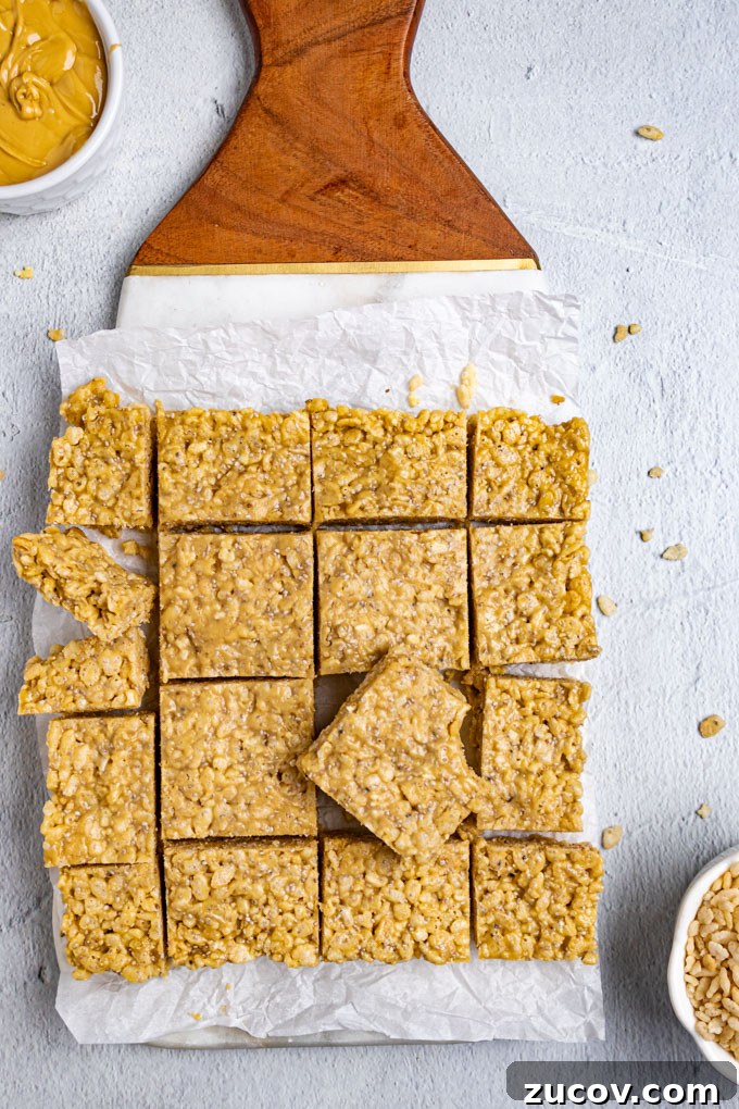 Rice Krispie Treats Without Marshmallows – Chewy Almond Butter Bars 2 Healthy rice krispie treats are cut up into squares and lying on a marble and wood board with parchment paper underneath. There is a bowl of cashew butter of to the side, along with a bowl of rice cereal.