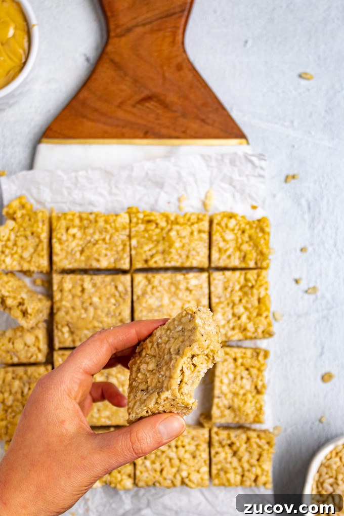 Rice Krispie Treats Without Marshmallows – Chewy Almond Butter Bars 5 Close up shot of healthy rice krispie treats. The treats are cut into squares, and a hand is holding one of the bars, with a bite taken out of it.