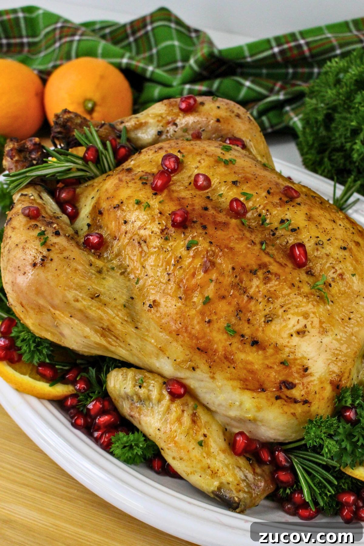 Succulent Roast Chicken Recipe for Christmas Dinner 2 Golden brown roasted chicken on a platter with pomegranate seeds and oranges as garnish.