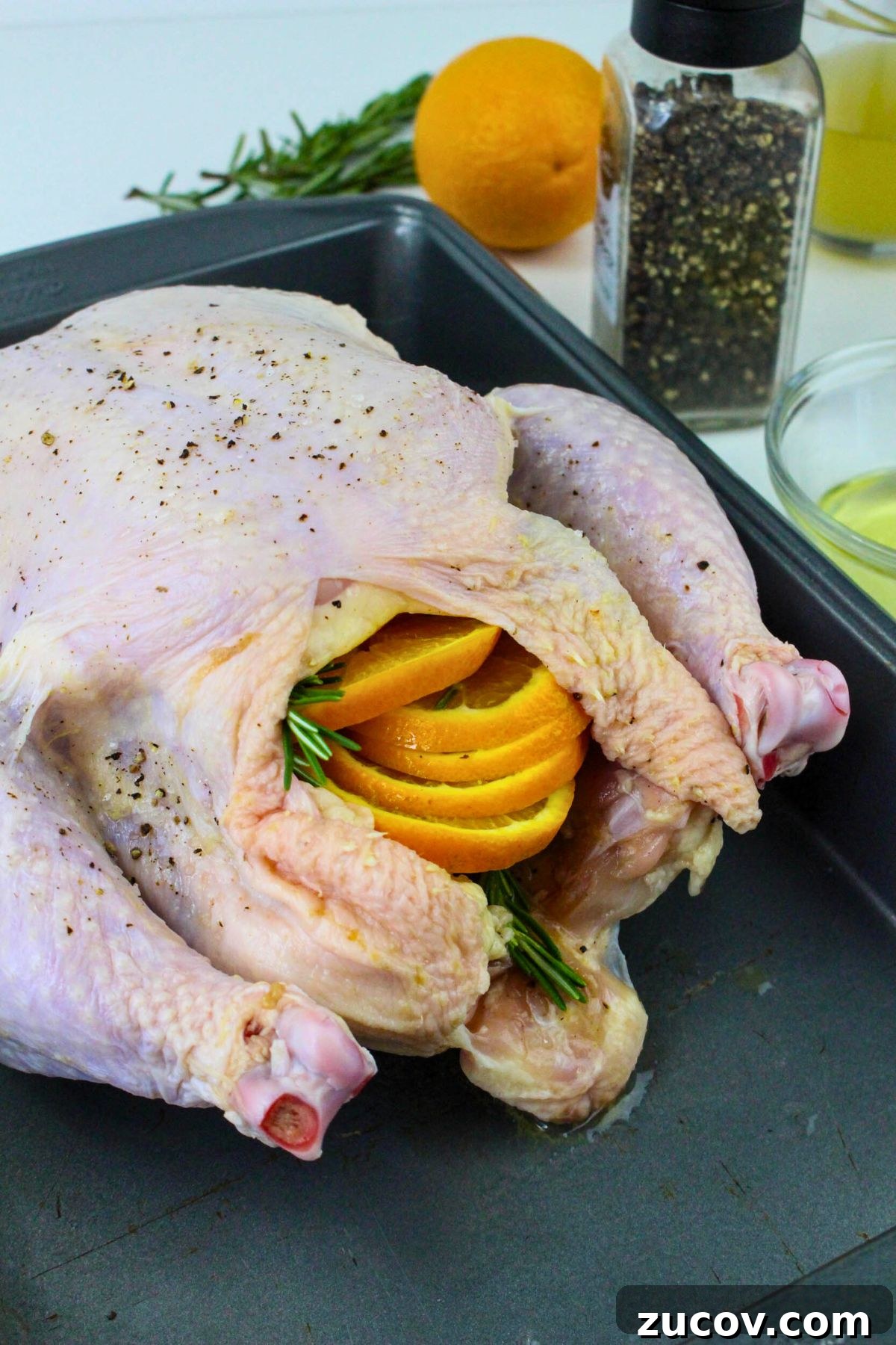 Succulent Roast Chicken Recipe for Christmas Dinner 4 Uncooked chicken stuffed with orange slices and seasonings in a roasting pan.