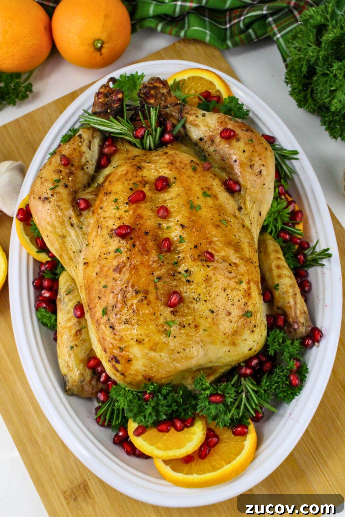 Succulent Roast Chicken Recipe for Christmas Dinner 8 Golden roasted chicken on a white platter with parsley and pomegranate seeds as garnish.