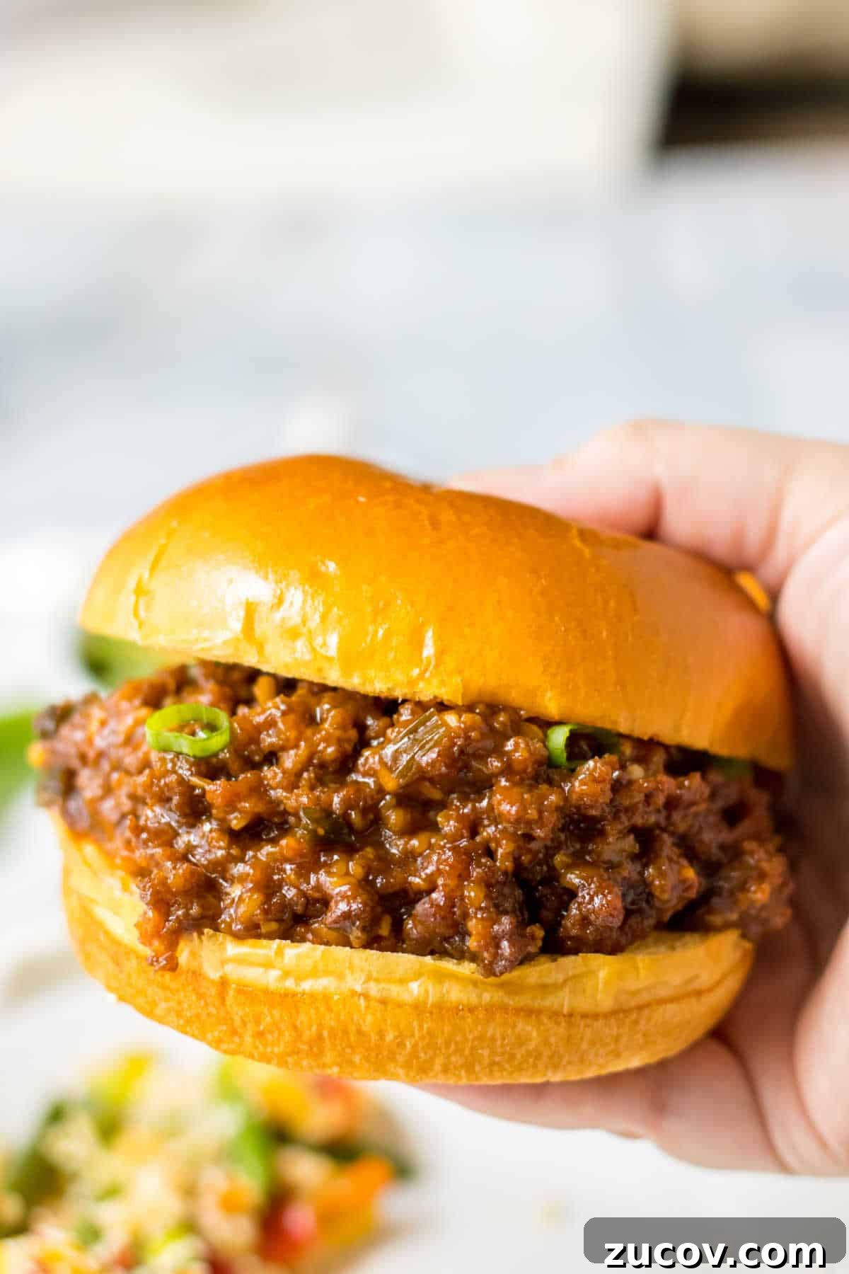 Korean-Style Sloppy Joes in the Slow Cooker: Tangy Gochujang Sandwiches 8 A hand holding a Korean sloppy joe.