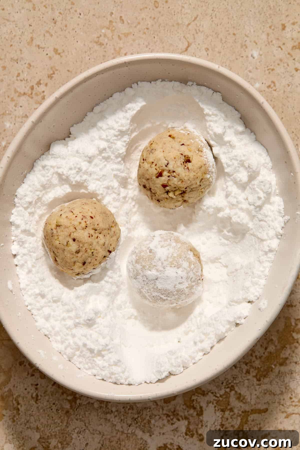 Cream Cheese Pecan Snowball Cookies for Christmas Baking 7 Snowball cookies rolled in powdered sugar in bowl.