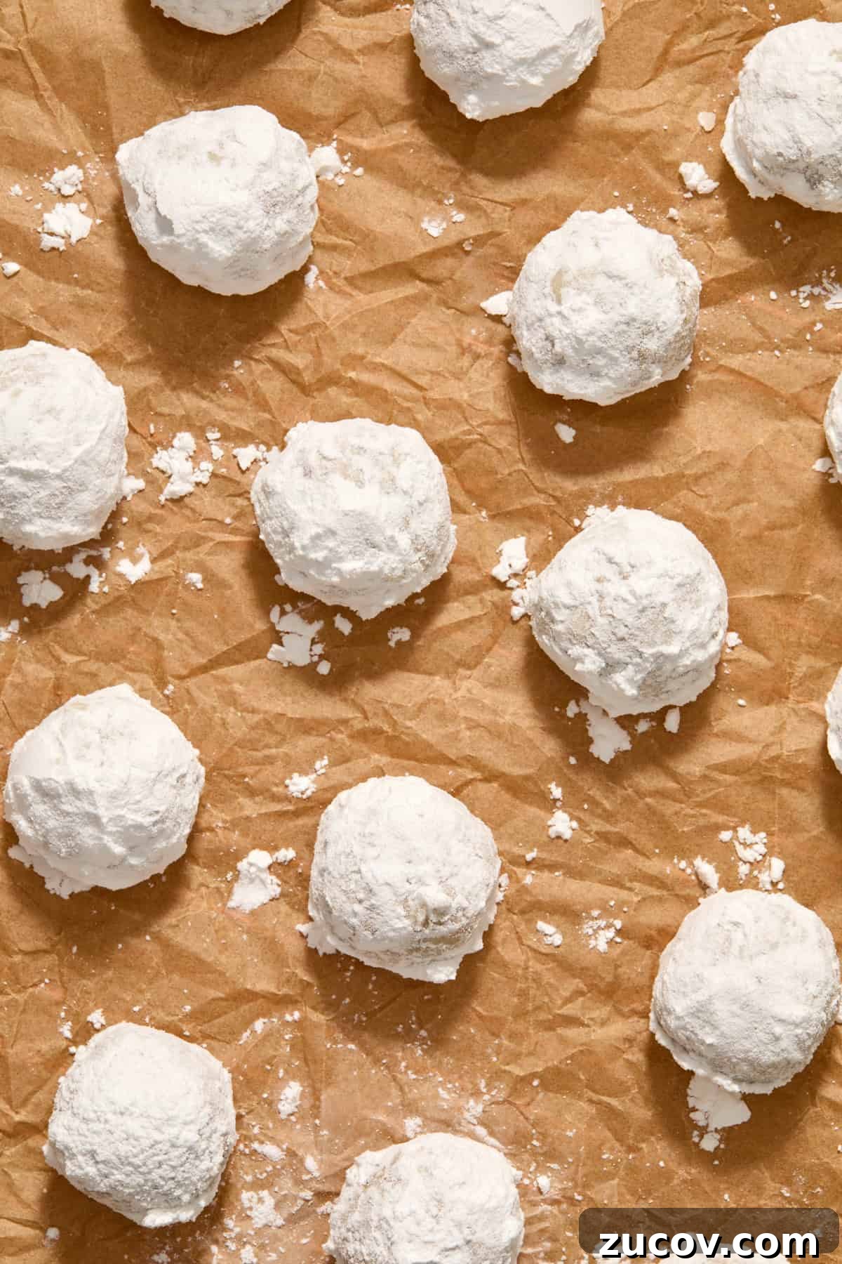 Cream Cheese Pecan Snowball Cookies for Christmas Baking 8 Parchment paper with powdered sugar covered cookies arranged.