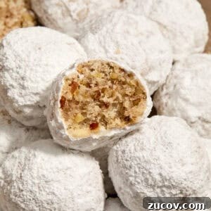 Cream Cheese Pecan Snowball Cookies for Christmas Baking 10 Pecan snowball cookies with powdered sugar on plate with bite taken out of one cookie.