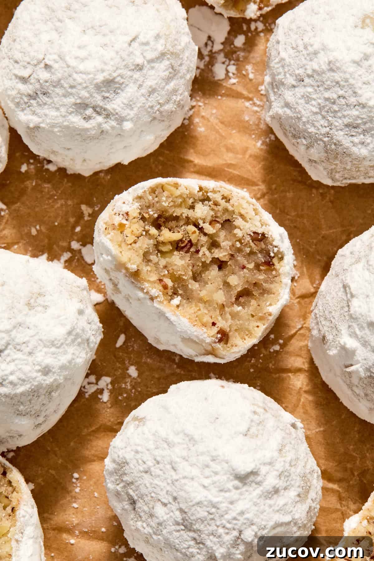Cream Cheese Pecan Snowball Cookies for Christmas Baking 3 Parchment paper with pecan snowball cookies arranged on top and bite taken from one cookie.