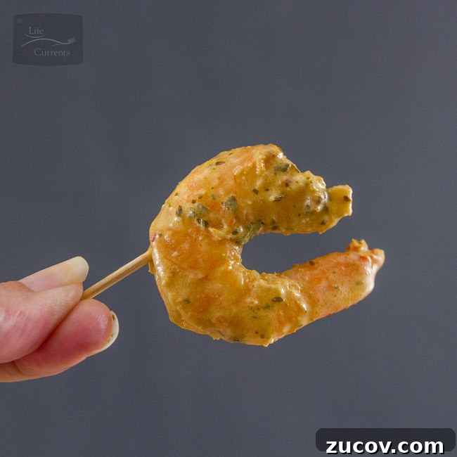 Creamy Pesto Shrimp Appetizer Recipe is super quick & easy & really delicious! Shrimp in sauce on a toothpick being held by a hand.