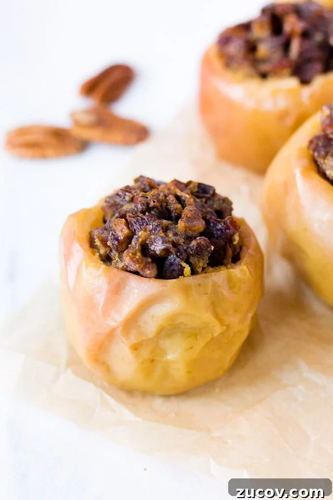 Paleo Baked Apples Recipe: Warm Spiced Fruit Dessert 2 a baked apple with filling inside and two on the right in the background. three pecans in the left background.