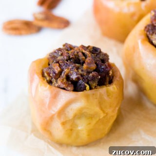 Paleo Baked Apples Recipe: Warm Spiced Fruit Dessert 5 a baked apple with filling inside and two on the right in the background. three pecans in the left background.
