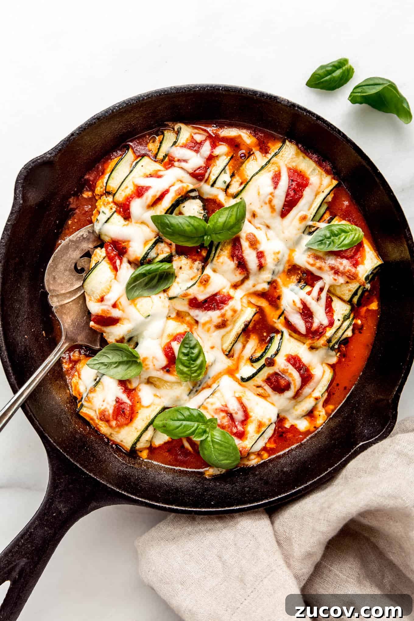 Ricotta-Stuffed Zucchini Roll-Ups with Tomato Basil Sauce 2 Zucchini involtini in a cast iron skillet topped with fresh herbs