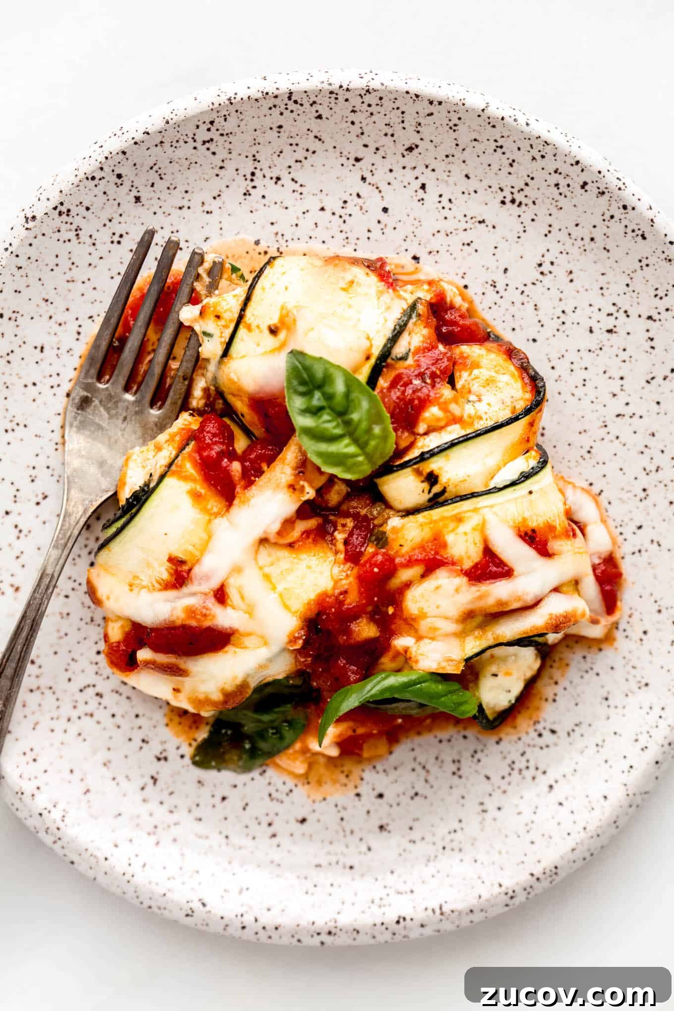 Ricotta-Stuffed Zucchini Roll-Ups with Tomato Basil Sauce 12 Zucchini involtini on a white speckled plate