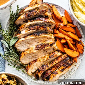 Crispy Juicy Air Fryer Turkey Breast Recipe 7 Sliced turkey breast on a serving platter with cooked carrots and fresh herbs.