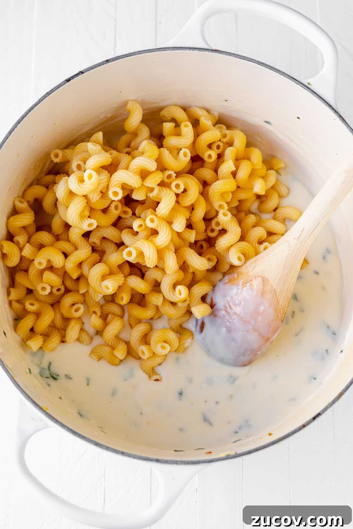 Tuscan Chicken Mac and Cheese Cavatappi noodles being added to the cheese sauce for tuscan chicken mac and cheese.