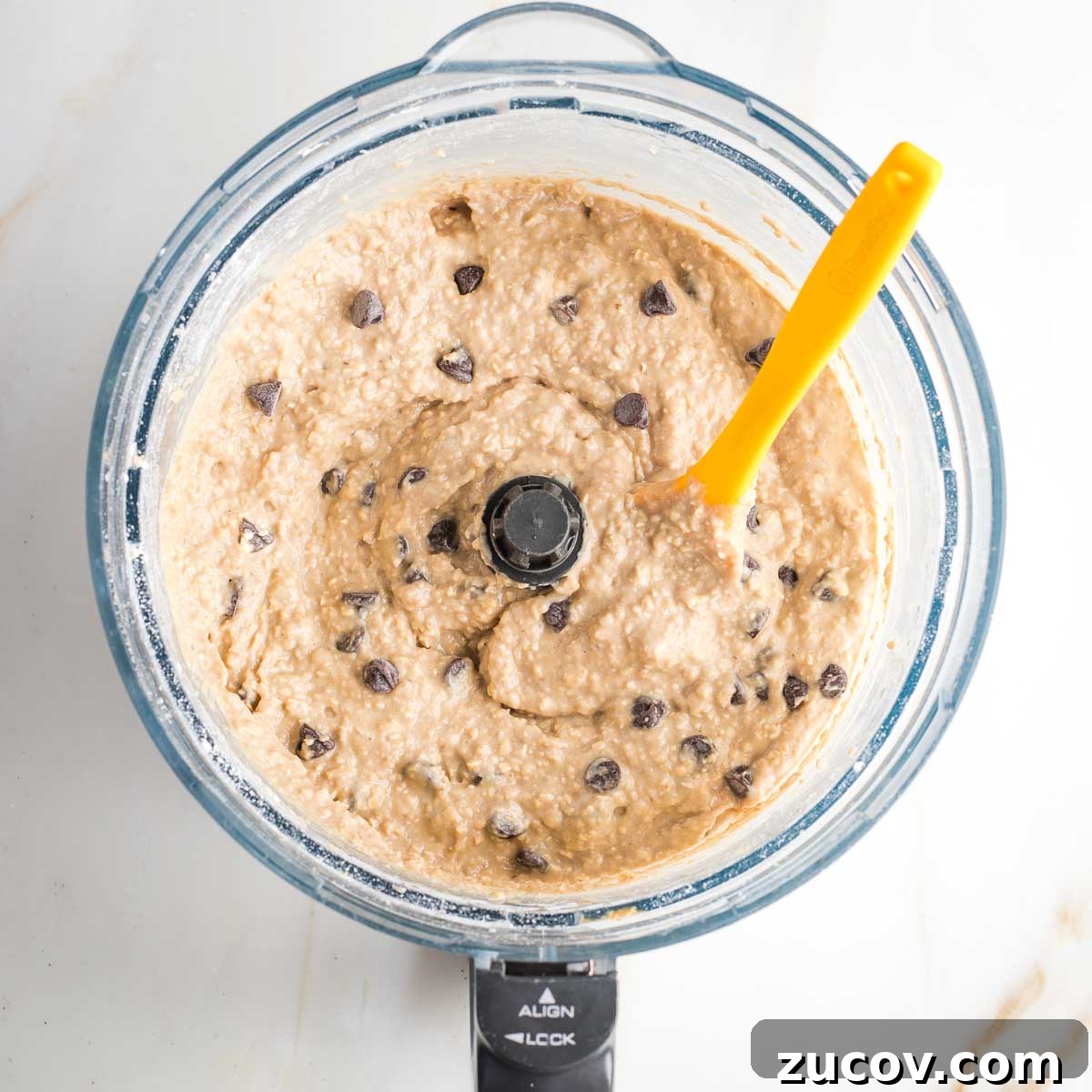 Vegan White Bean Blondies: Chewy, Protein-Packed Treats 10 Spatula mixing chocolate chips into blondie batter in the bowl of a food processor.