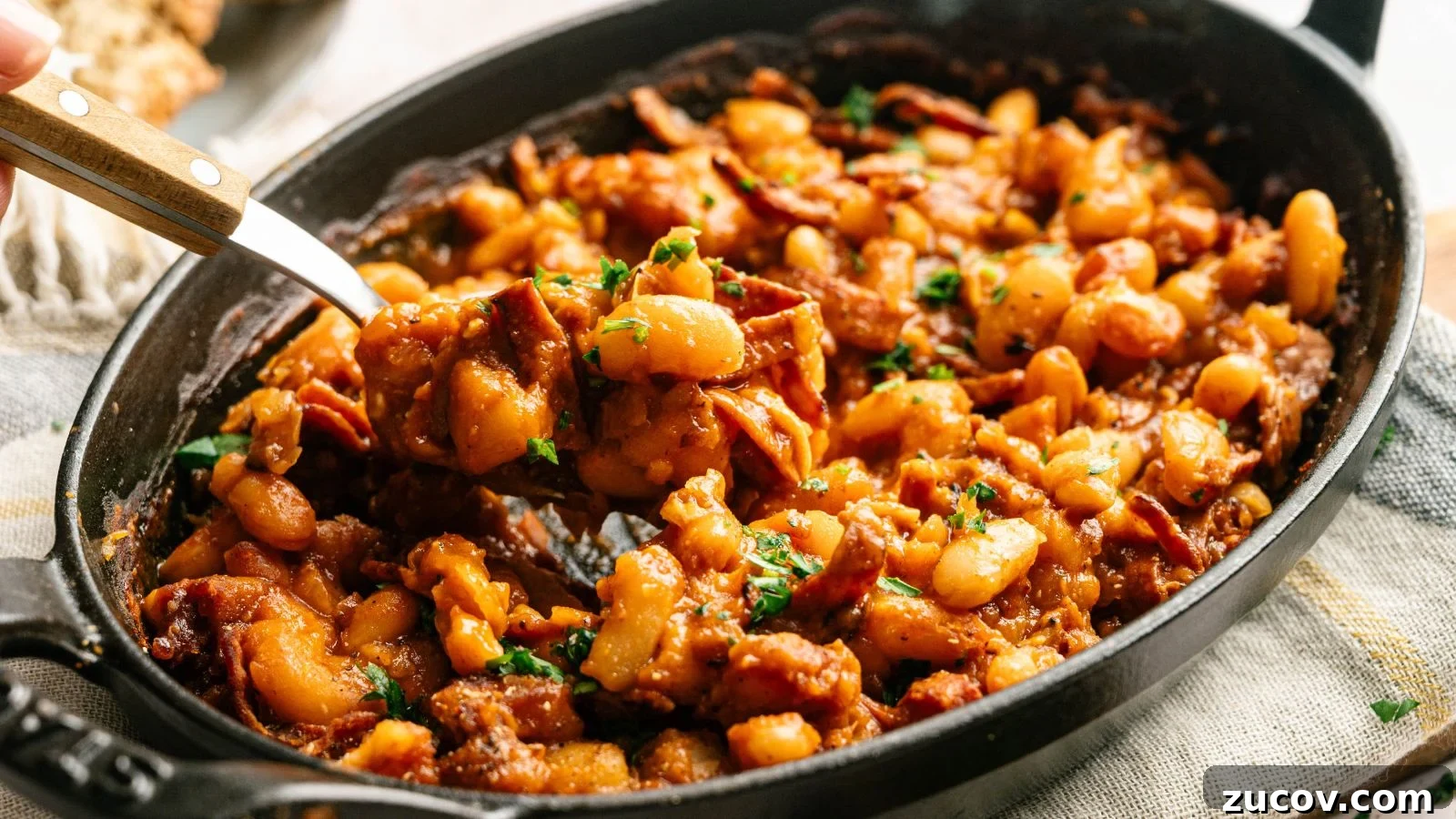 21 Summer Budget Meals That Make Takeout Obsolete 13 A black oval dish filled with baked beans in a rich sauce, mixed with pieces of bacon and garnished with chopped parsley.