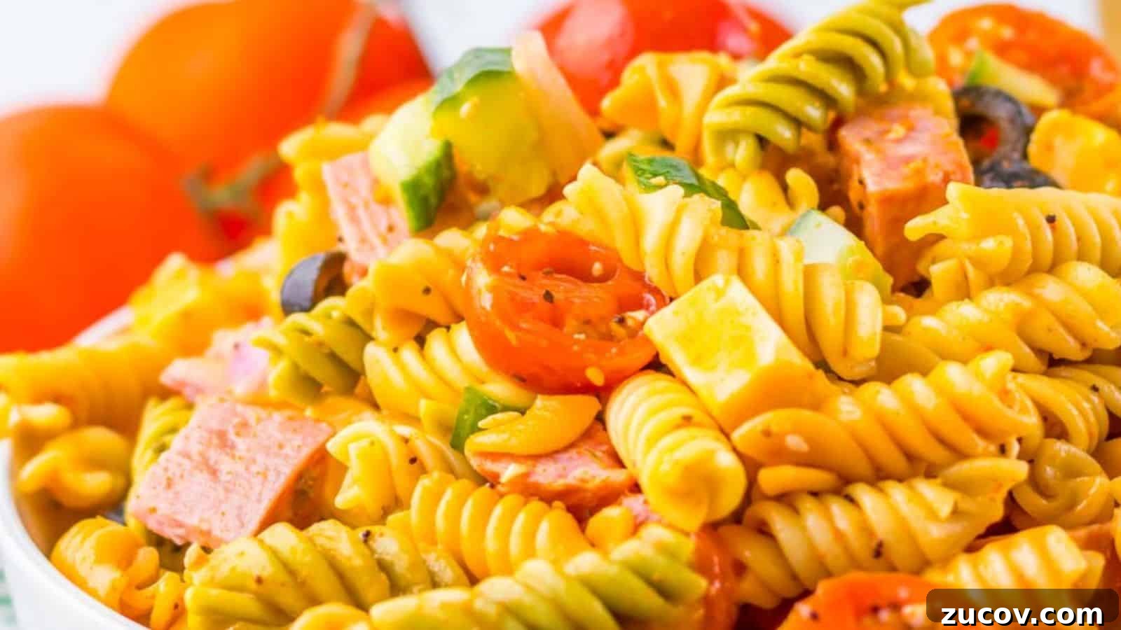 21 Summer Budget Meals That Make Takeout Obsolete 3 A vibrant pasta salad with fusilli, cherry tomatoes, bell peppers, black olives, and diced salami in a clear bowl.