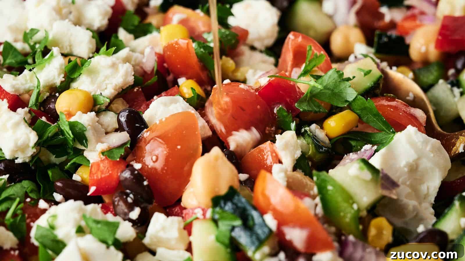 21 Summer Budget Meals That Make Takeout Obsolete 21 Close-up of a mixed salad with tomatoes, feta cheese, black beans, chickpeas, corn, cucumber, red onion, and parsley, being drizzled with dressing.