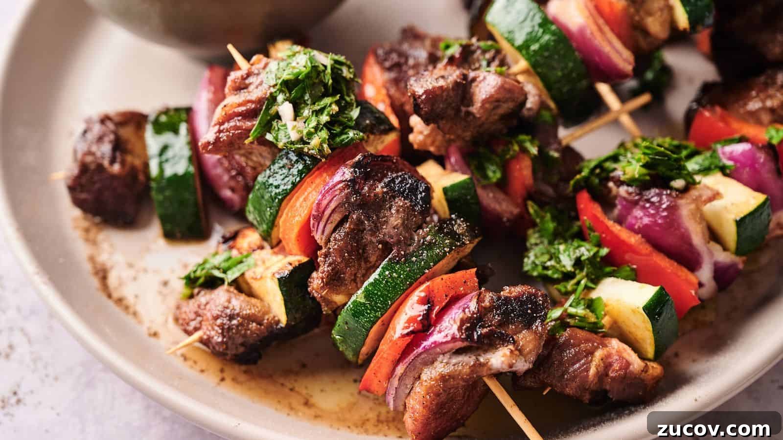 21 Summer Budget Meals That Make Takeout Obsolete 7 Grilled meat and vegetable skewers with zucchini, red onion, and red bell pepper, garnished with chopped herbs, served on a beige plate.