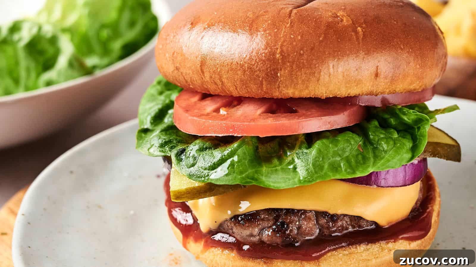 21 Summer Budget Meals That Make Takeout Obsolete 8 A cheeseburger with lettuce, tomato, pickles, onion, and ketchup on a plate. A bowl of lettuce is in the background.