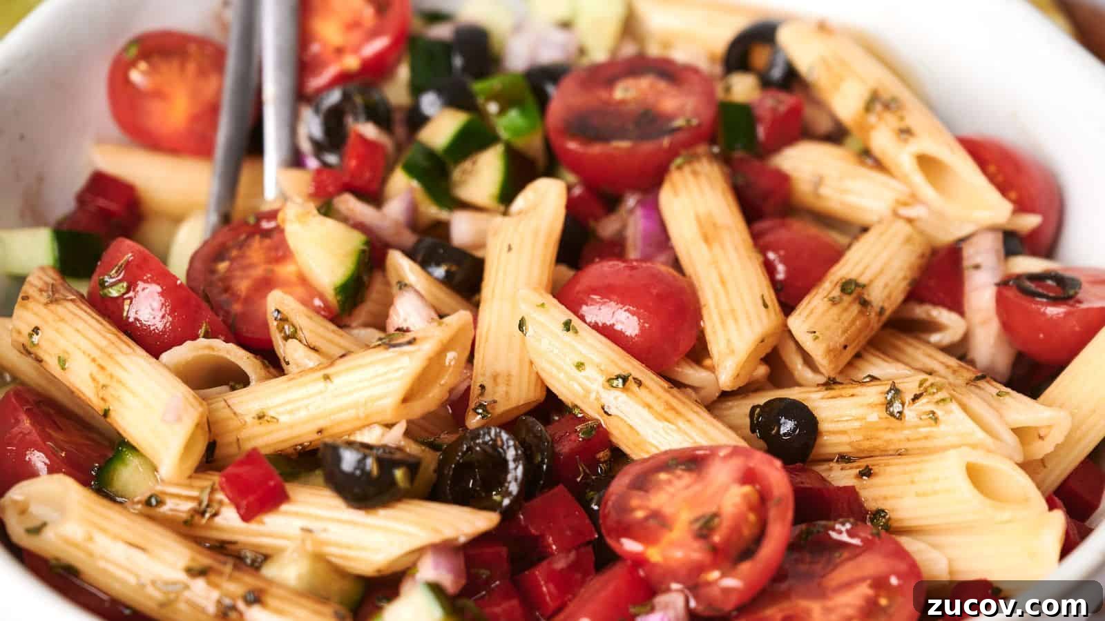 21 Summer Budget Meals That Make Takeout Obsolete 9 A bowl of vibrant pasta salad with penne, cherry tomatoes, black olives, diced cucumbers, red onions, and a drizzle of dressing.
