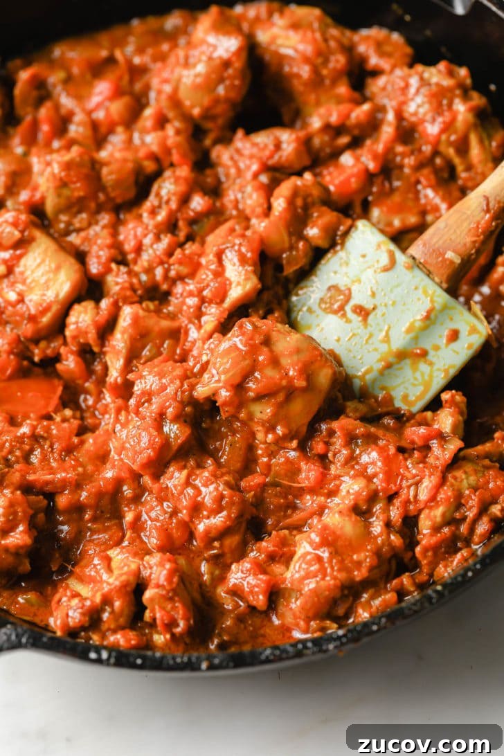 Authentic Chicken Jalfrezi Recipe: Spicy Tangy Curry at Home 9 Tomatoes added to chicken thighs in a black skillet
