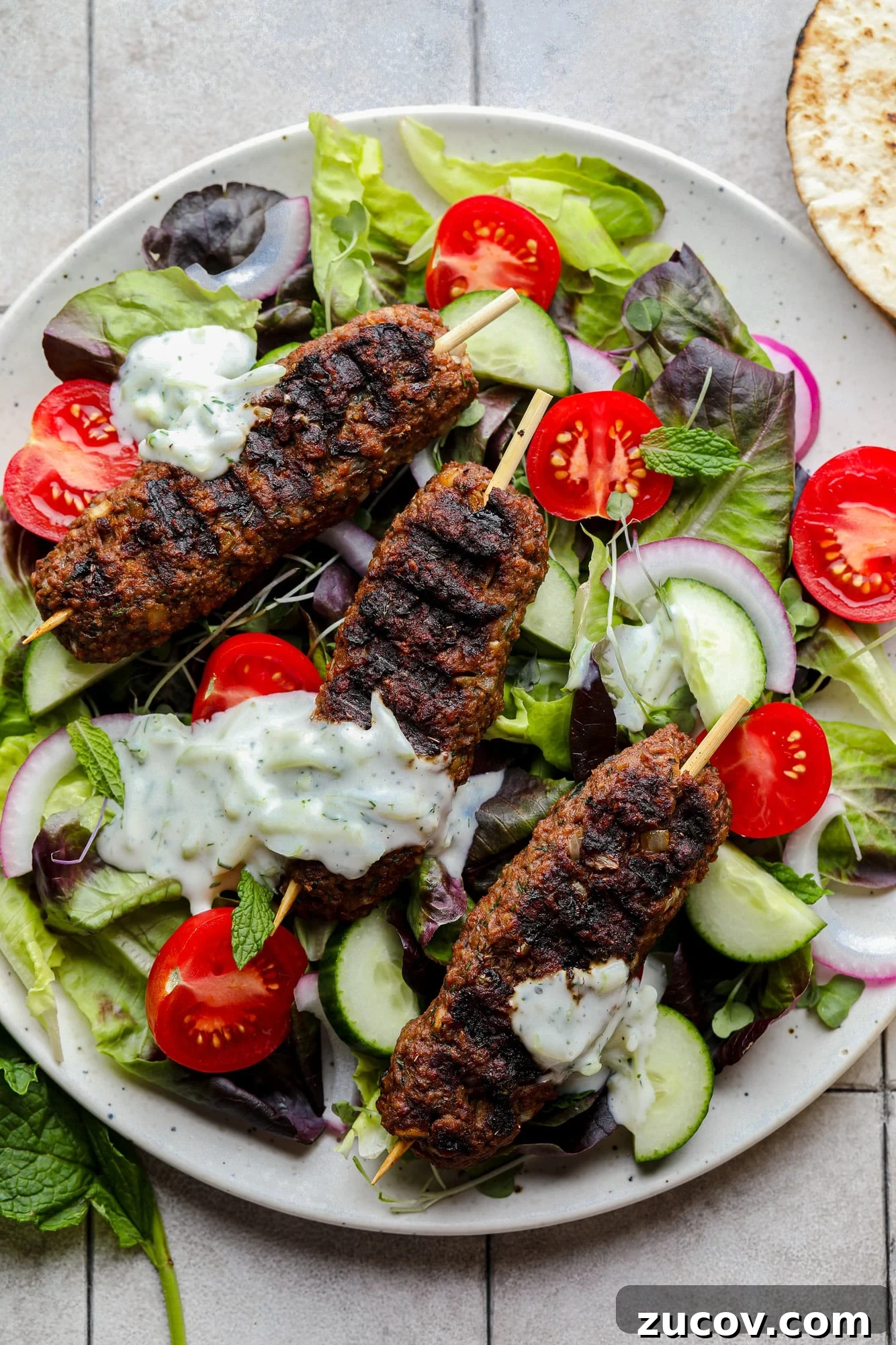 Vegan Kofta Recipe: Flavorful Plant-Based Meatballs 2 grilled vegan kofta on top of a green salad with vegetables and tzatziki.