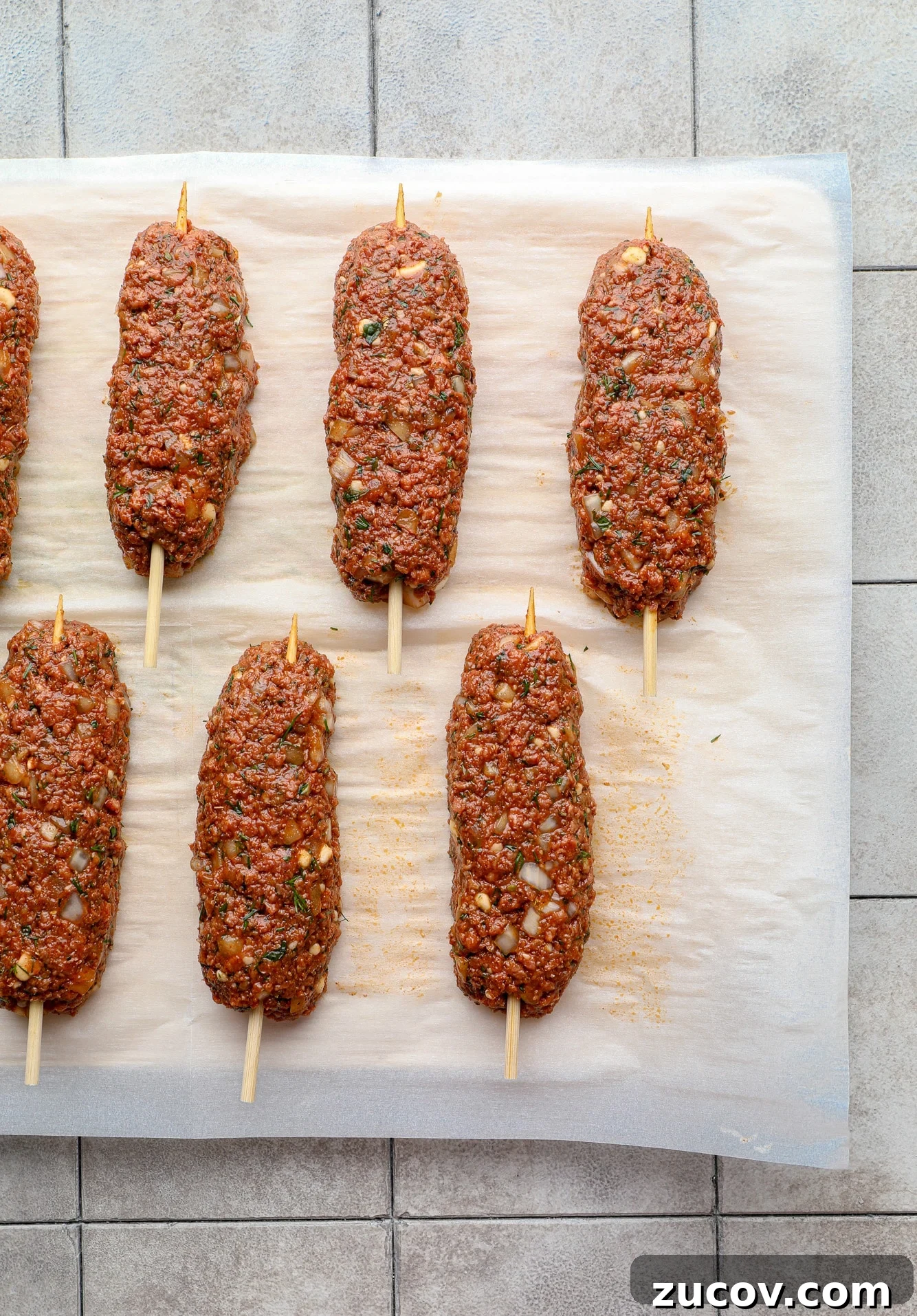 Vegan Kofta Recipe: Flavorful Plant-Based Meatballs 7 uncooked vegan kofta on wooden skewers on a parchment-lined baking sheet.