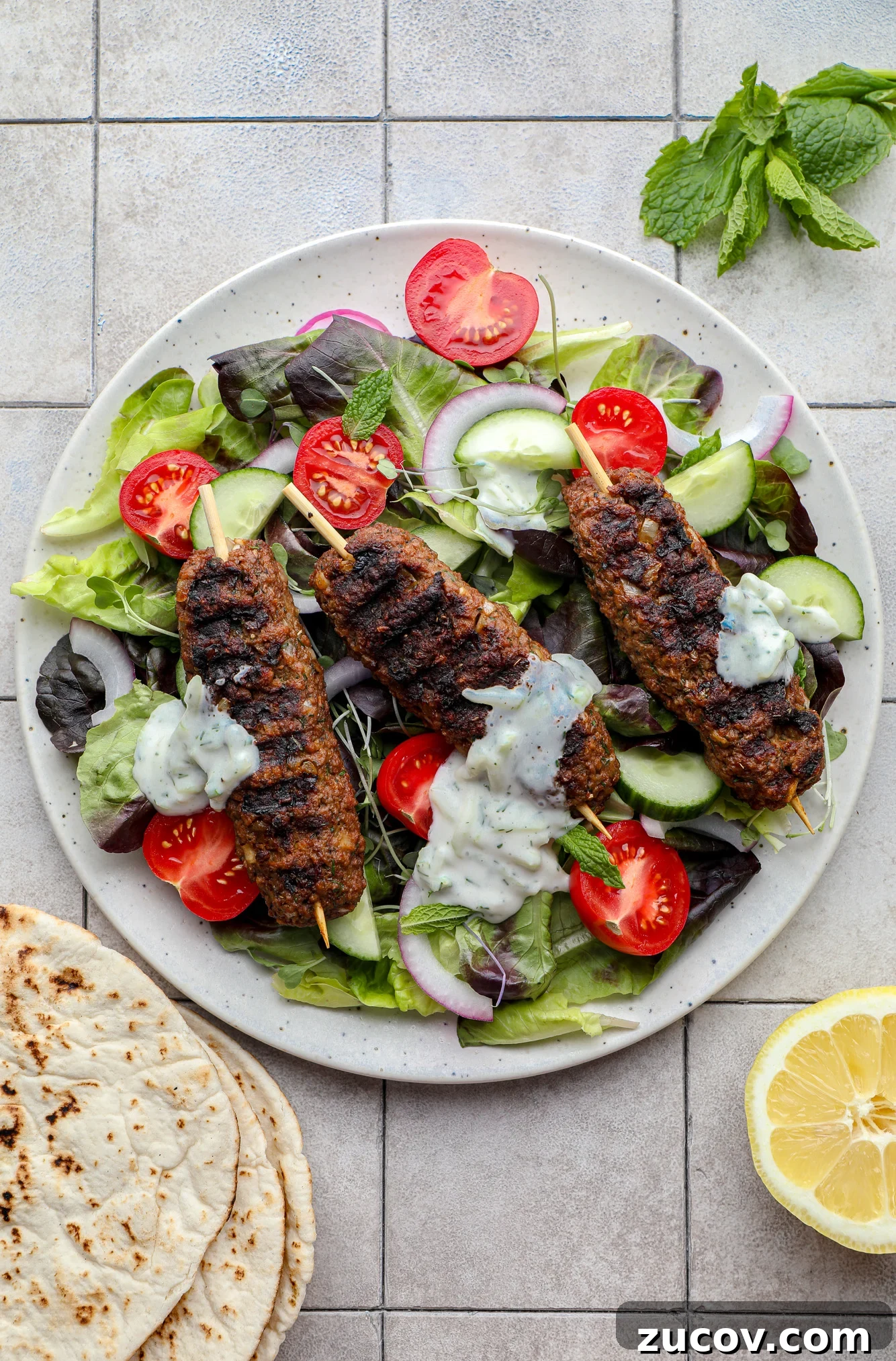 Vegan Kofta Recipe: Flavorful Plant-Based Meatballs 9 grilled vegan kofta on top of a green salad with vegetables and tzatziki.