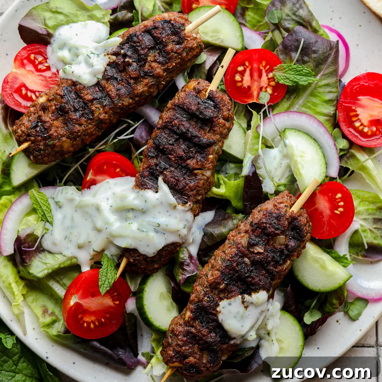 Vegan Kofta Recipe: Flavorful Plant-Based Meatballs 10 grilled vegan kofta on top of a green salad with vegetables and tzatziki.