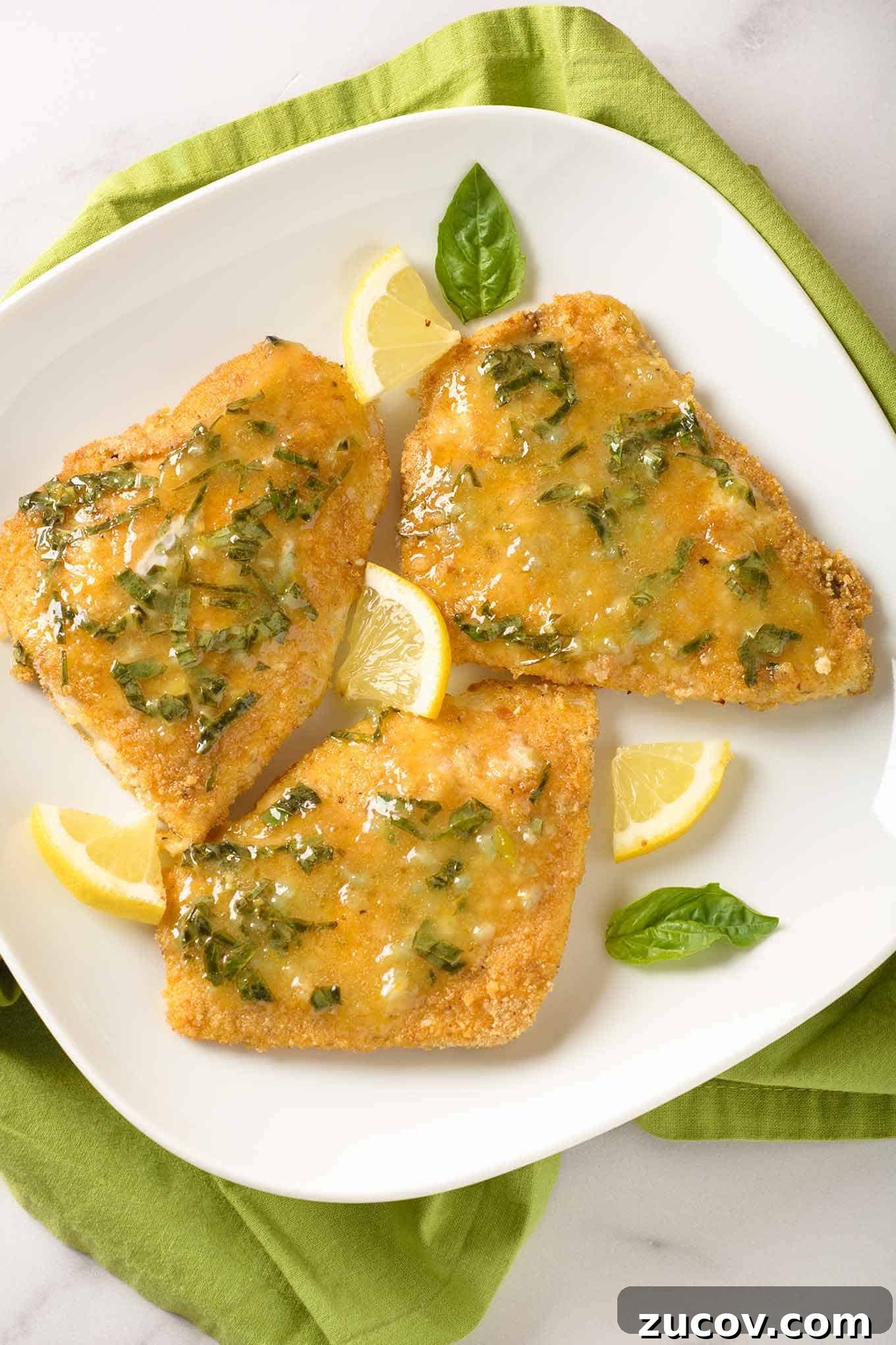 Lemon Basil Butter Oven-Fried Fish Recipe 2 Three pieces of breaded, oven-fried fish fillets topped with lemon butter infused with fresh basil and garnished with basil leaves and lemon wedges.