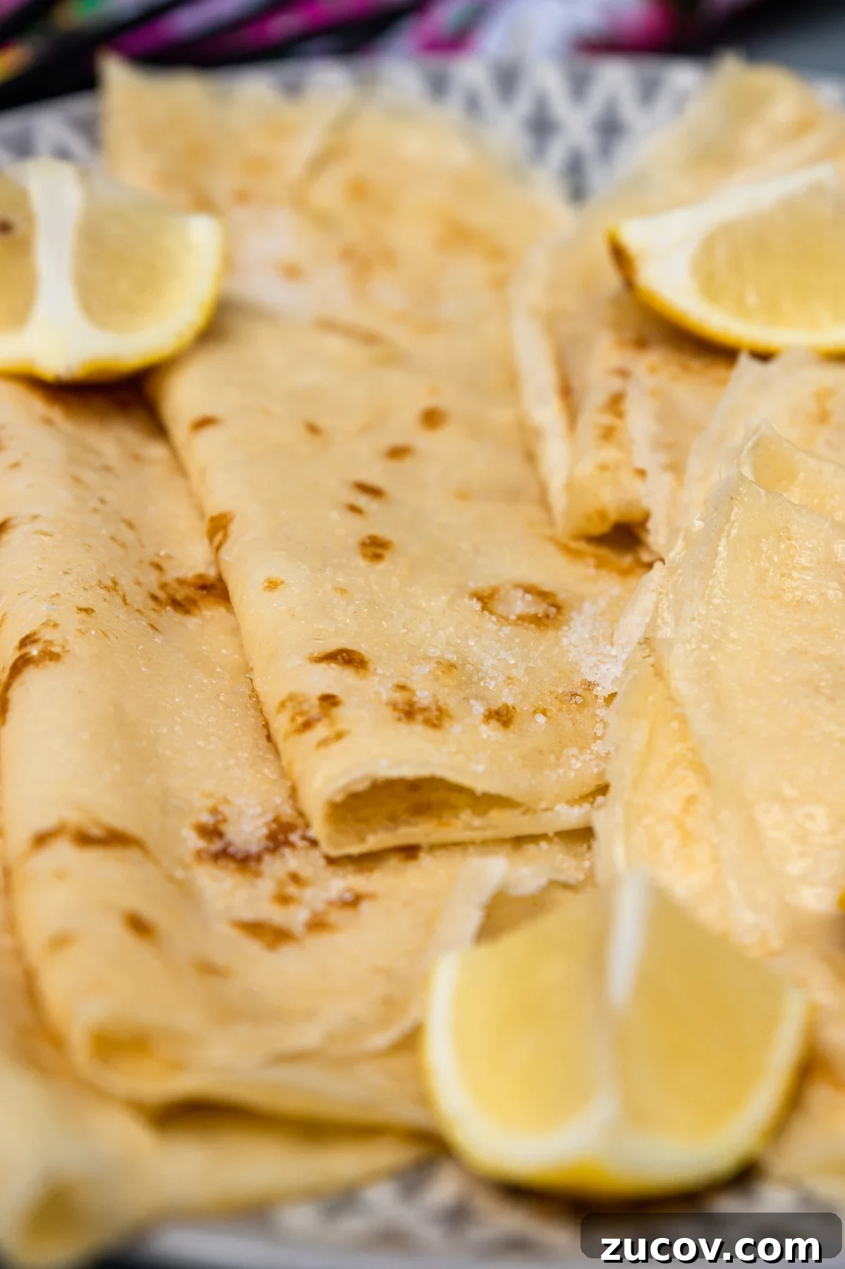 Crisp Lemon Sugar English Pancakes Recipe 6 Closeup of thin English pancakes on a grey and white plate with sugar and lemon on top