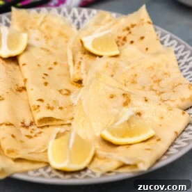 Closeup of plate of English pancakes on grey and white plate, blue background and with colourful tea towel and whisk