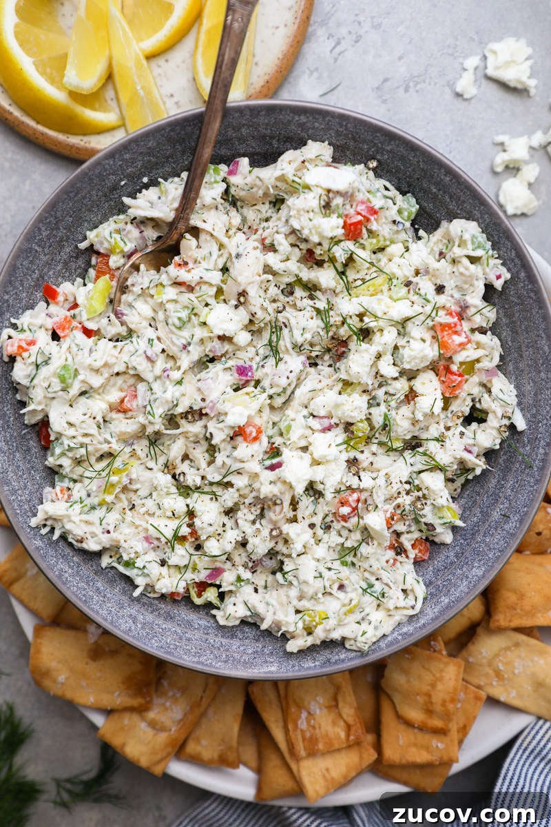 Greek-Style Feta Chicken Salad with Lemon-Dill Dressing 2 A blue serving bowl filled with feta chicken salad sitting next to pita chips and fresh lemon wedges