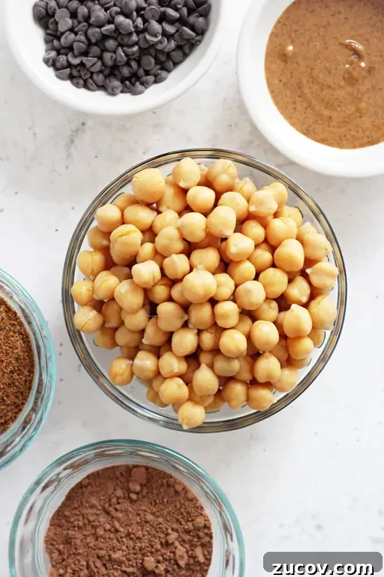 This brownie hummus is made with a few simple ingredients like chickpeas, coconut sugar, almond butter and cocoa powder. Small bowls filled with chickpeas, almond butter, chocolate chips and cocoa powder.