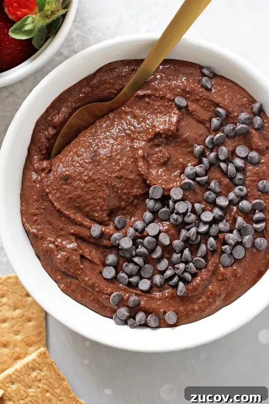 Made with pantry staples, this 10-minute brownie batter hummus satisfies chocolate cravings without the guilt. A white bowl filled with Brownie Batter Hummus with a gold spoon in the dish.