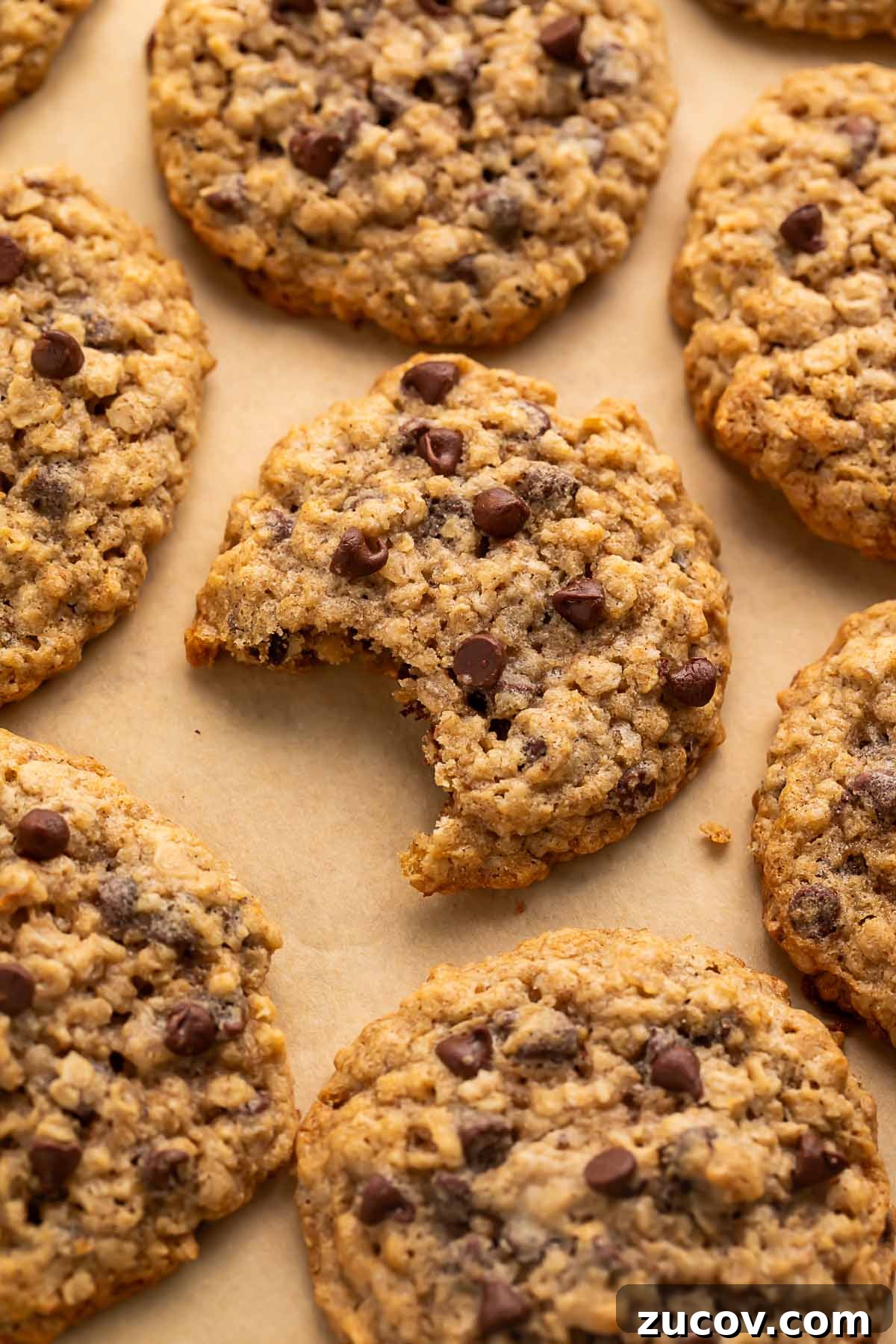 Gluten-Free Oatmeal Chocolate Chip Cookies Recipe 2 Close-up of gluten free oatmeal chocolate chip cookies arranged on a sheet of parchment paper, with a bite missing from the center cookie.