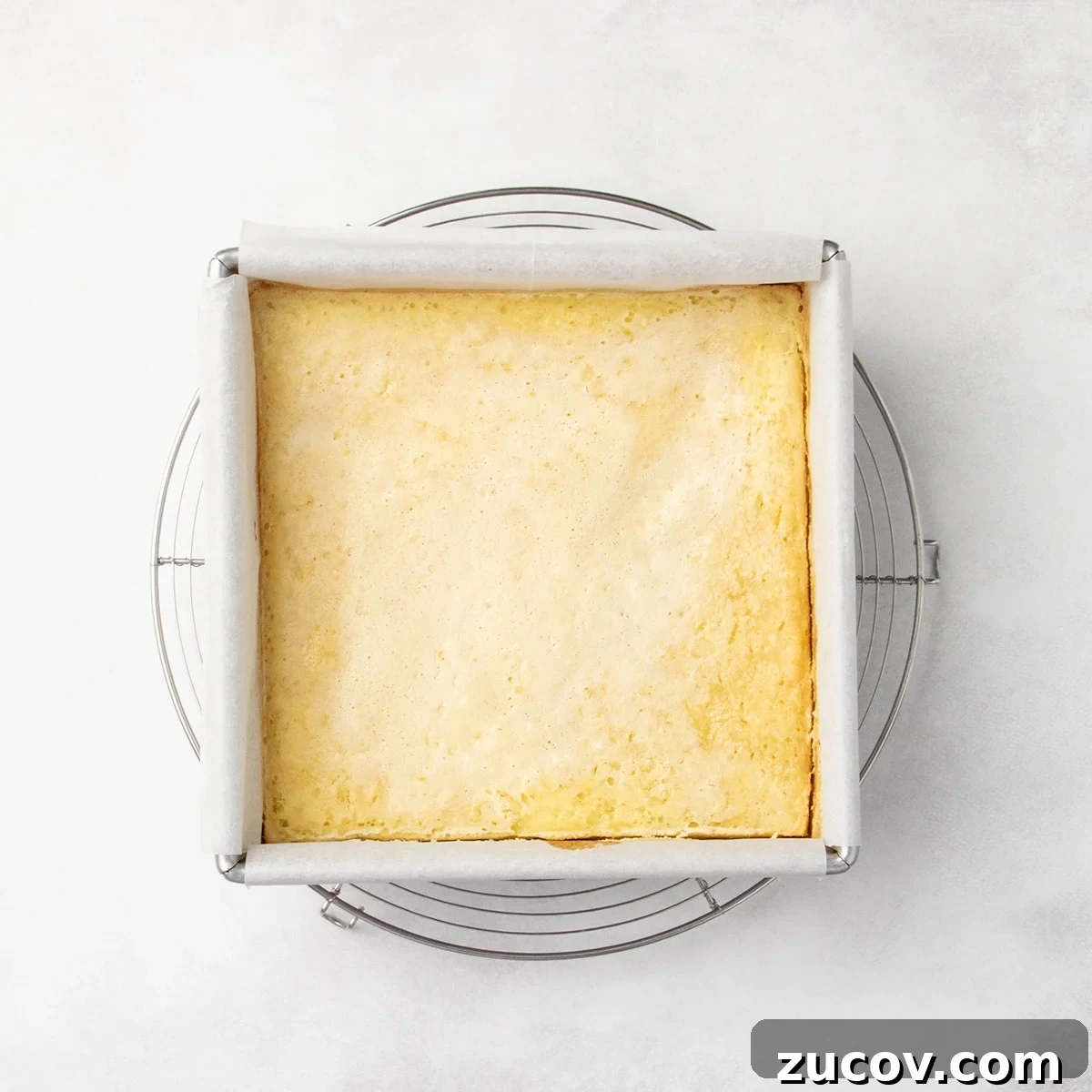 Gluten-Free Lemon Bar Recipe: Zesty, Tart Citrus Squares 16 Uncut, baked lemon bars in a parchment-lined square pan resting on a round wire rack, lightly golden around the edges.
