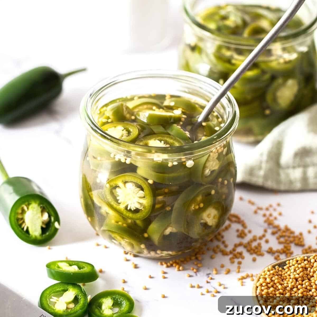 Jar of pickled jalapeños with a spoon sitting in jar, with some fresh jalapeños around the edge.