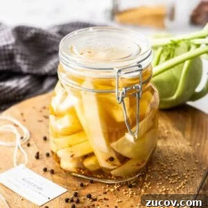 Crispy Pickled Kohlrabi Recipe for Tangy, Quick Ferments 14 Jar of Pickled Kohlrabi, sitting on a round wooden board, with some herbs and spices around the edge.