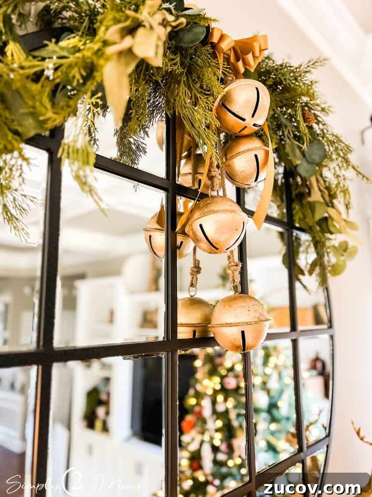 13 Elegant Christmas Fireplace Decorating Ideas to Try This Year 7 Large gold jingle bells strung on rope hanging over a round mirror with greenery for Christmas.