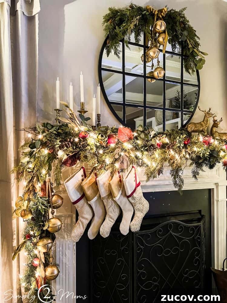 13 Elegant Christmas Fireplace Decorating Ideas to Try This Year 10 Fireplace with asymmetrical Christmas garland, stockings, round mirror with greenery half wreath at night.