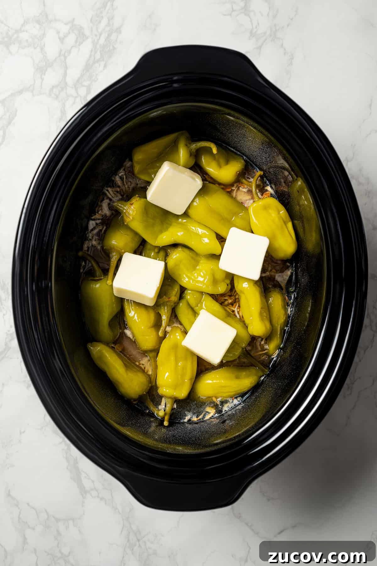 Mississippi Chicken Recipe: Slow Cooker & Oven Methods 7 Pats of butter placed over top pepperoncini peppers and chicken inside the crock pot.
