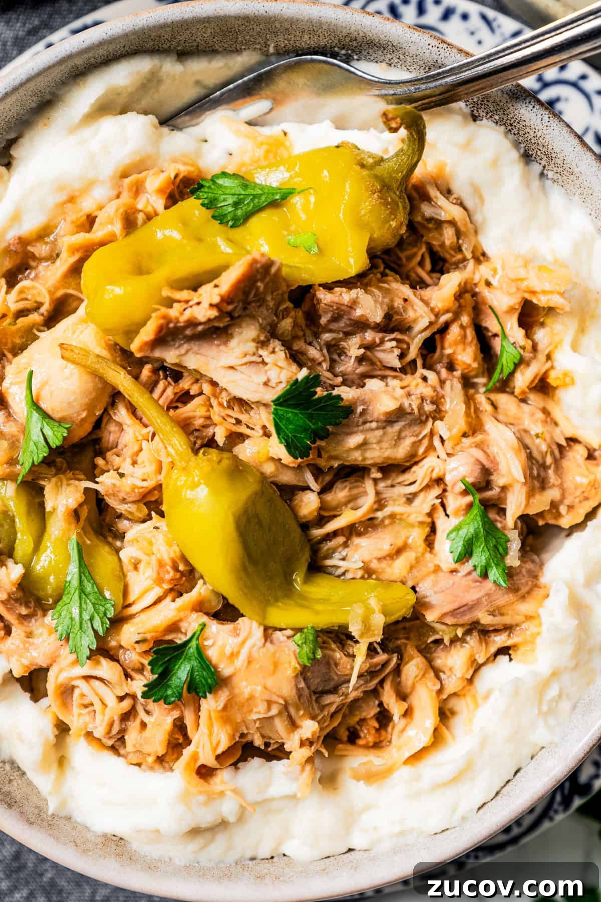 Mississippi Chicken Recipe: Slow Cooker & Oven Methods 9 Close-up photo of shredded Mississippi chicken and pepperoncini served over mashed potatoes.