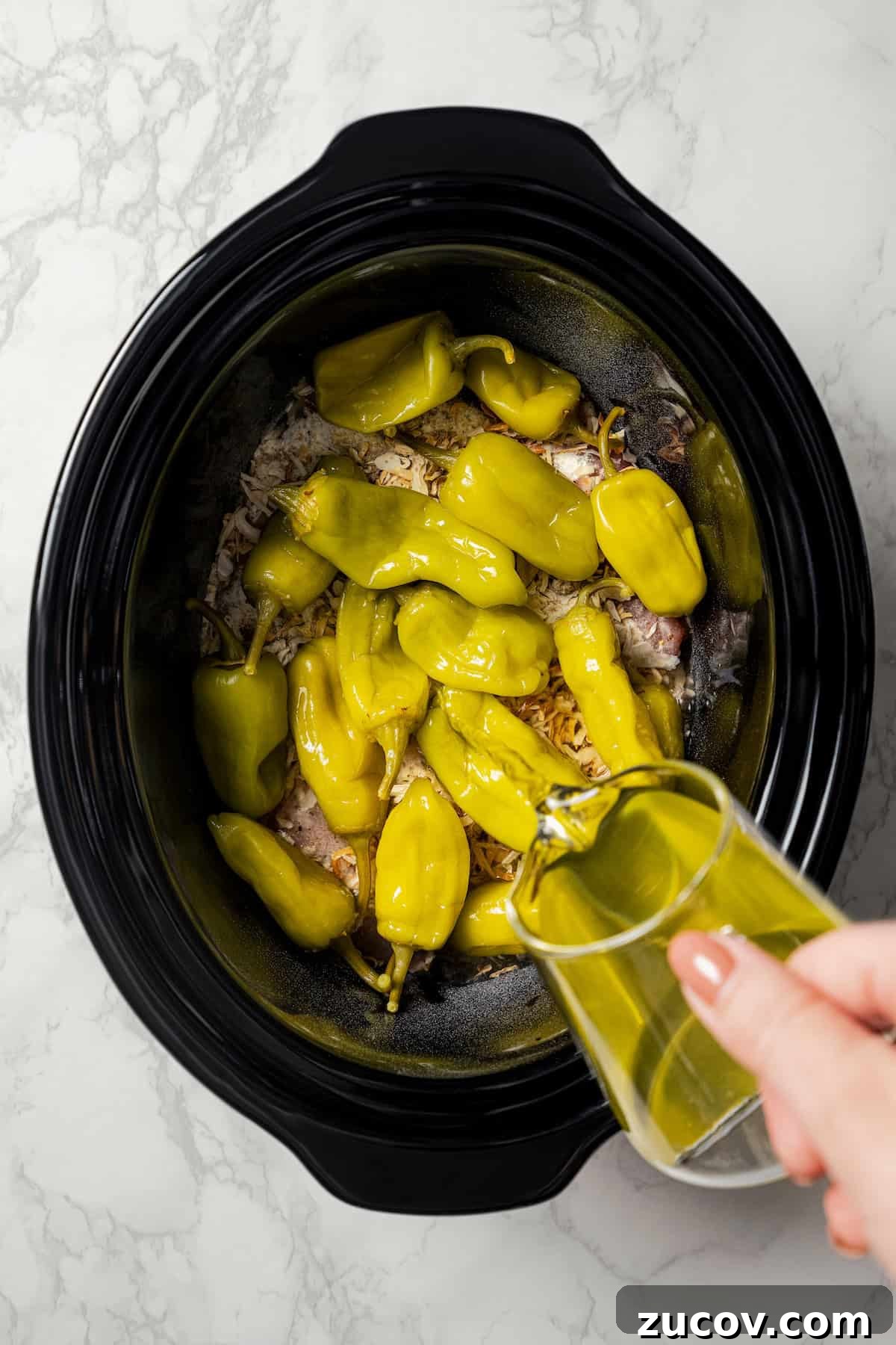 Mississippi Chicken Recipe: Slow Cooker & Oven Methods 6 Pepperoncini juice being poured over the peppers and chicken inside the crock pot.