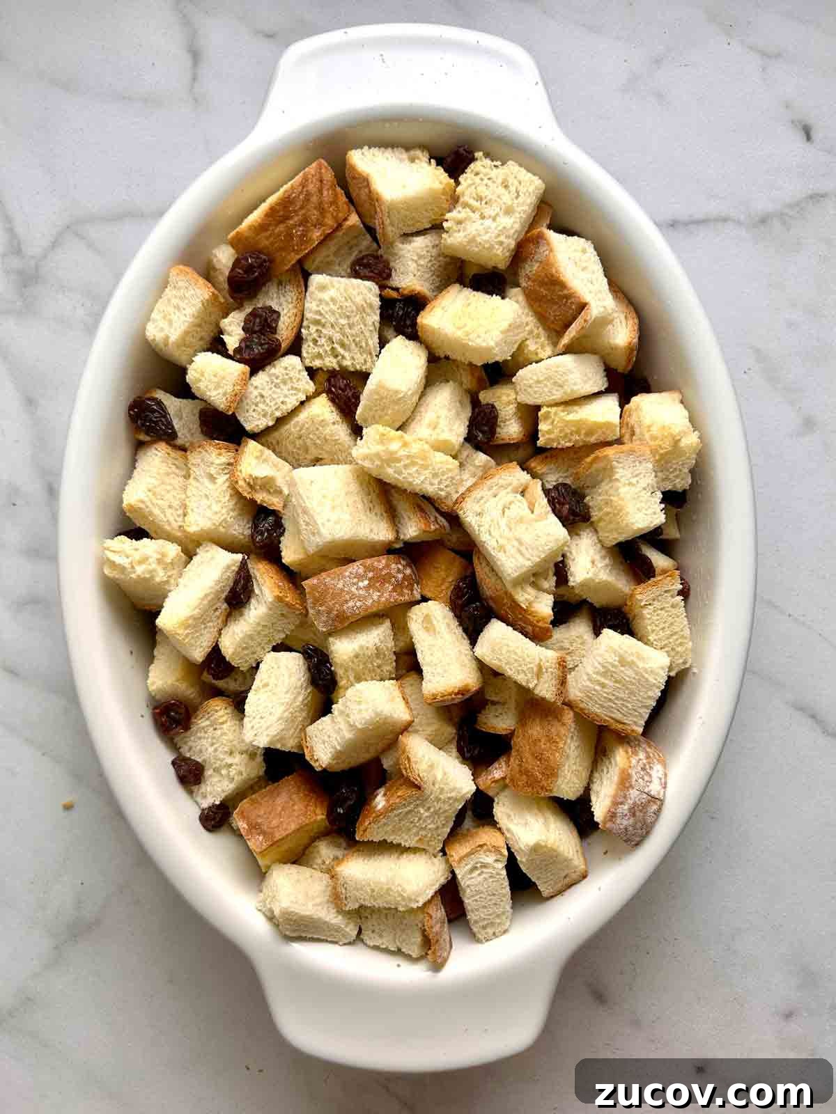 Classic Bread Pudding Recipe with Caramel Sauce and Vanilla 4 bread cubes and raisins added to baking dish.