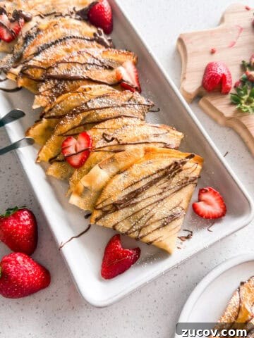 Strawberry Nutella crepes stacked on a plate.