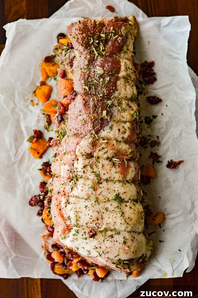 Fruit-Stuffed Pork Loin Roast with Apple and Cranberry Filling 7 A rolled up pork loin roast with stuffed fruit in it and fresh herbs sprinkled on top.