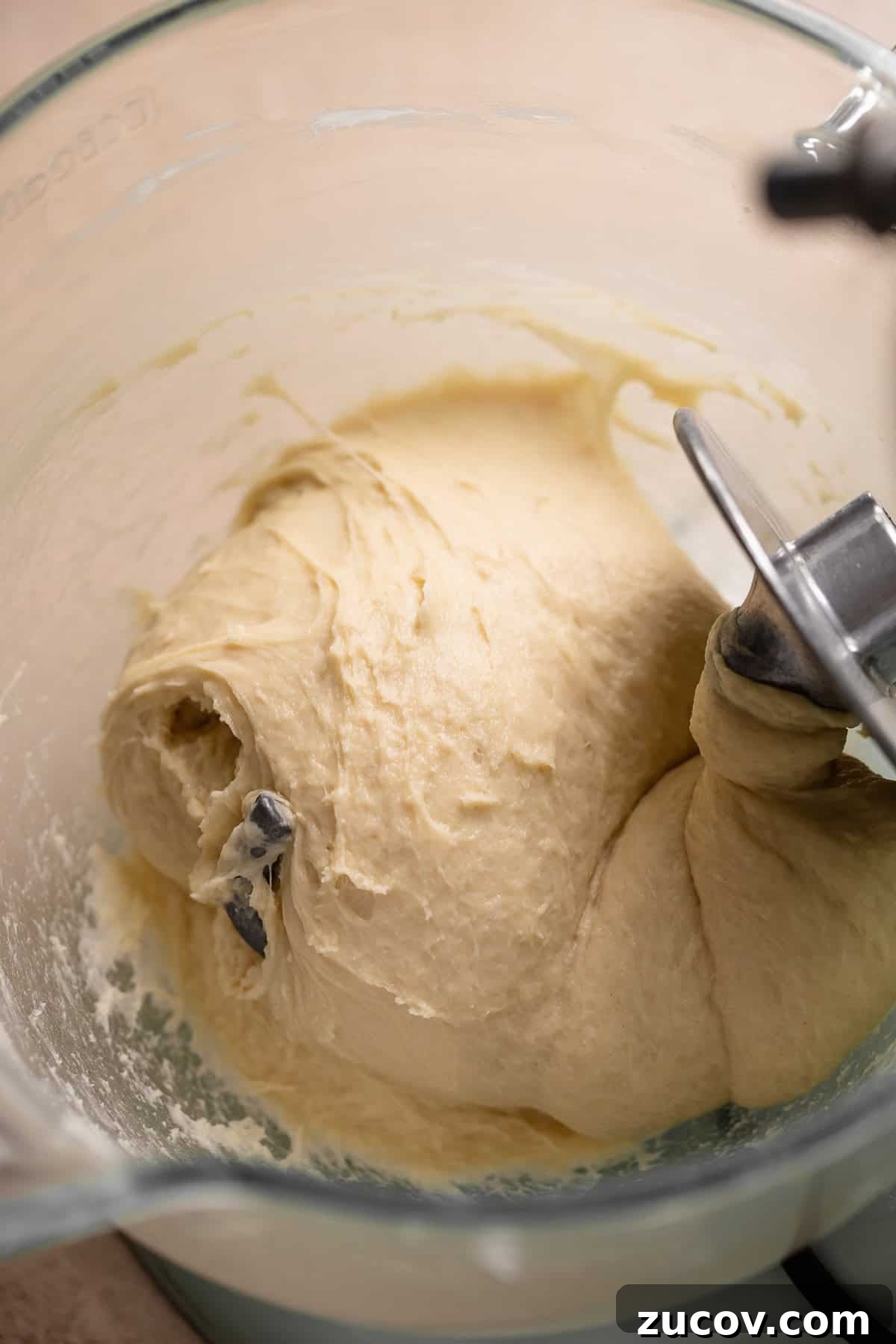Kneaded donut dough in a glass mixer bowl.