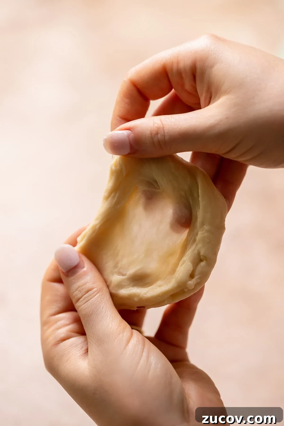 Two hands holding a piece of donut dough to show the gluten windowpane.